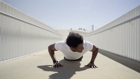 Focused-sporty-young-man-doing-push-ups-on-bridge.